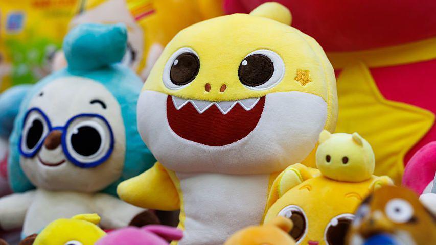 A row of Pinkfong's Baby Shark character soft toys on a display. The main yellow Baby Shark sits at the centre.