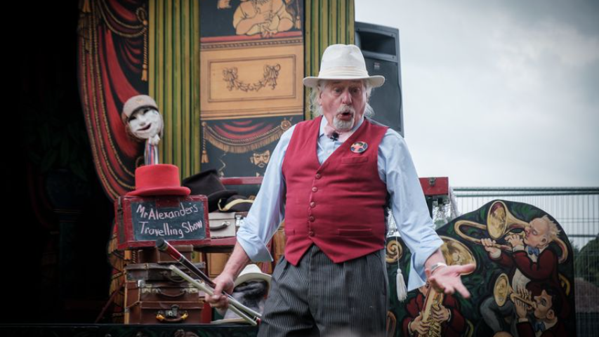 Images from BunkFest 2024 of a gentleman on stage doing a drama performance. He is wearing a white hat and a red waistcoat.
