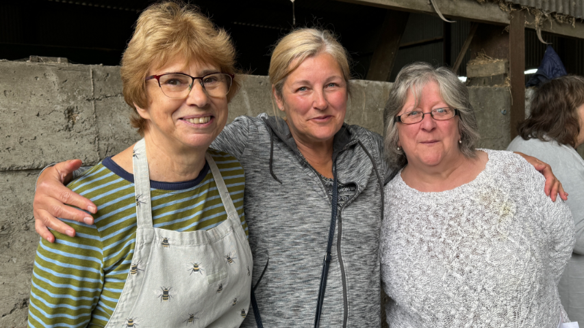 Three women standing with their arms around eachother at a farm