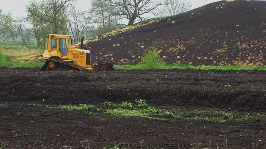 A yellow digger in front of a pile of compost in a field of peat