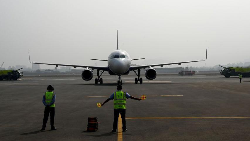An airport ground crew standing on a runway in front of a white aircraft 