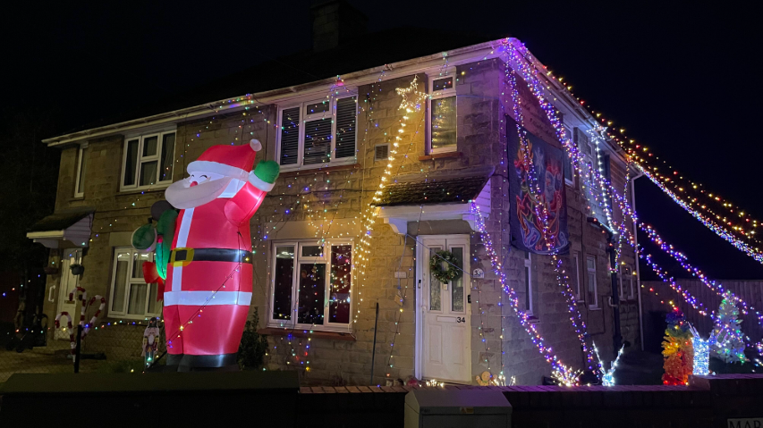 Giant inflatable Santa in the front garden of a house with streams of lights falling down the house into the garden.
