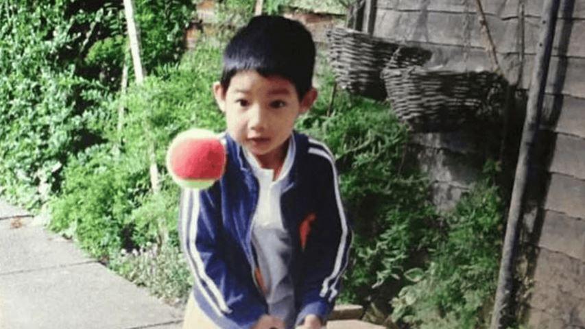 A young child with short dark hair in a blue top, standing in a garden looking at a large ball in the air
