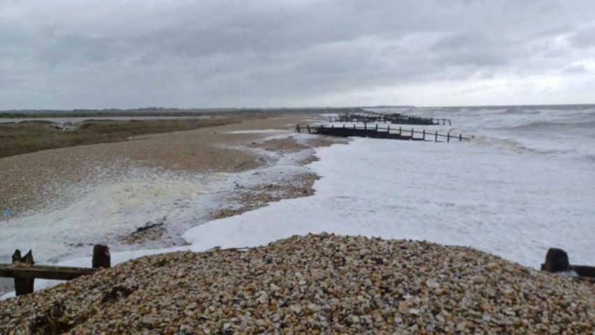 A shingle beach with heavy waves and foam rising up it
