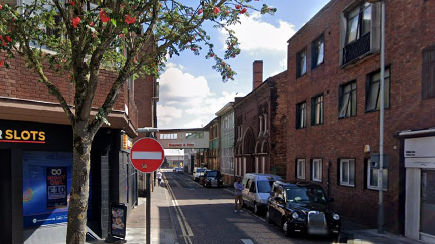 A city street with cars parked down one side and buildings on either side