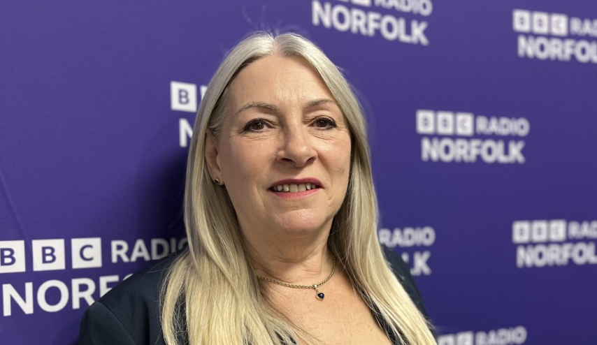 Kay Mason Billig with backdrop of blue screen with BBC Radio Norfolk repeated across it in white letters