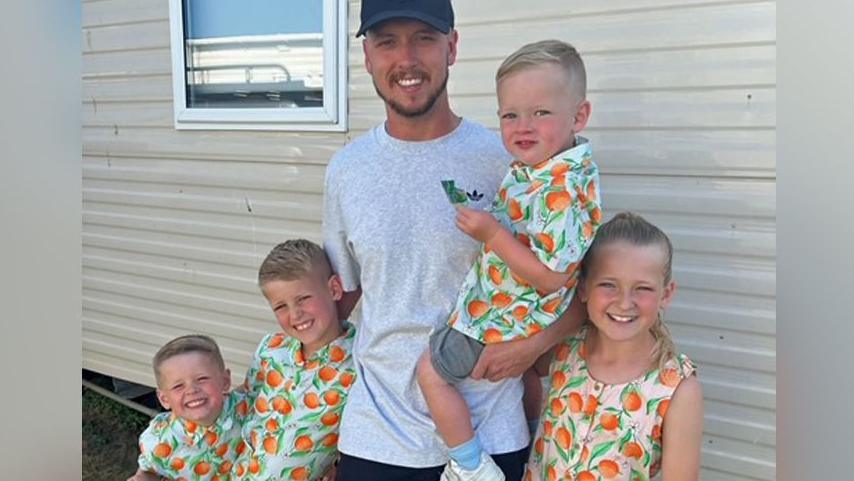 Nathan Osman standing with his four children who are all wearing matching fruit tops and shorts. All are smiling at the camera