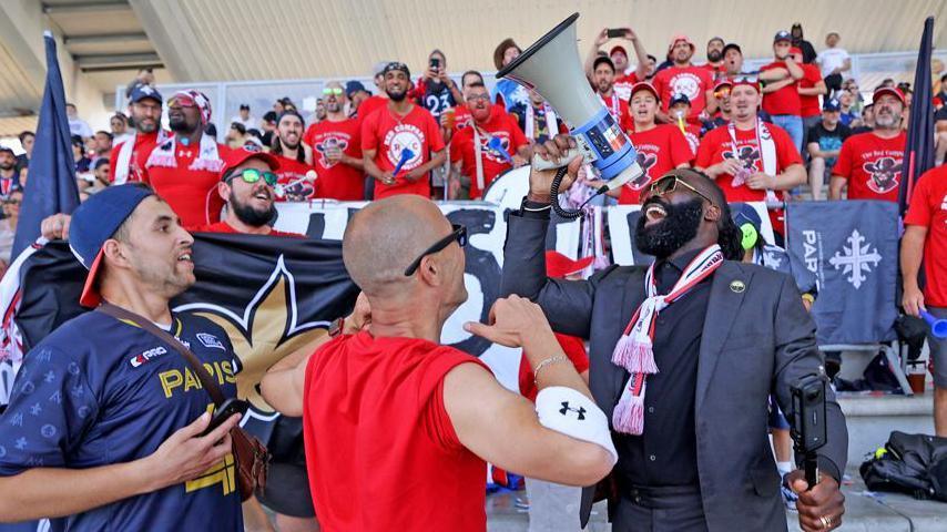 Demario Davis shouts into a megaphone surrounded by fans astatine a Paris Musketeers game