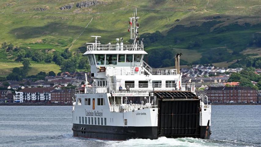 A ferry sailing through waters, with the coast of Largs in the background