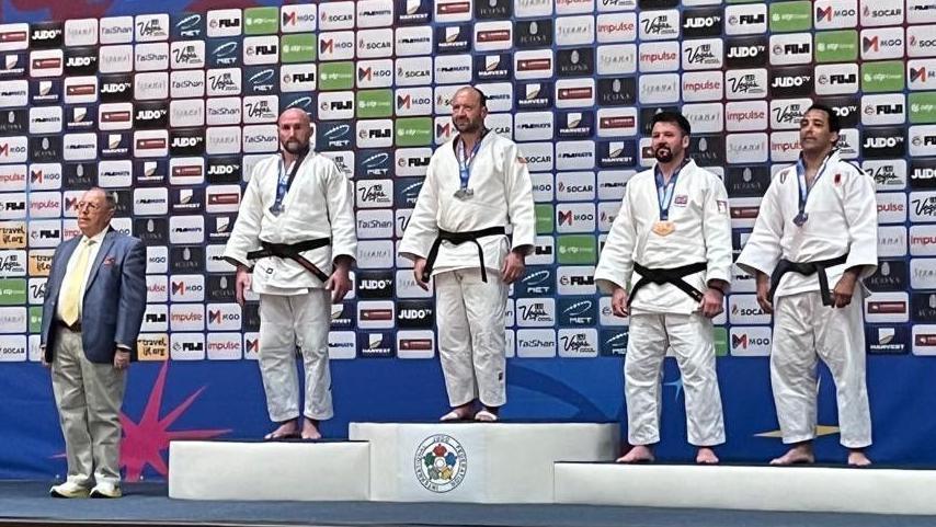 Shaun Mitty standing on the podium after winning gold.
He is wearing his judo uniform alongside three other men who are standing on the silver and bronze podiums.