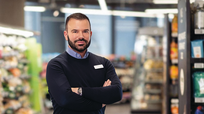 M&S Chief executive Stuart Machin in navy jumper and shirt, standing with arms folded inside store