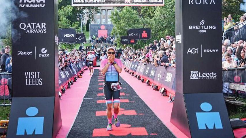 A woman dressed in athletic clothing crosses the finish line at an Ironman challenge.