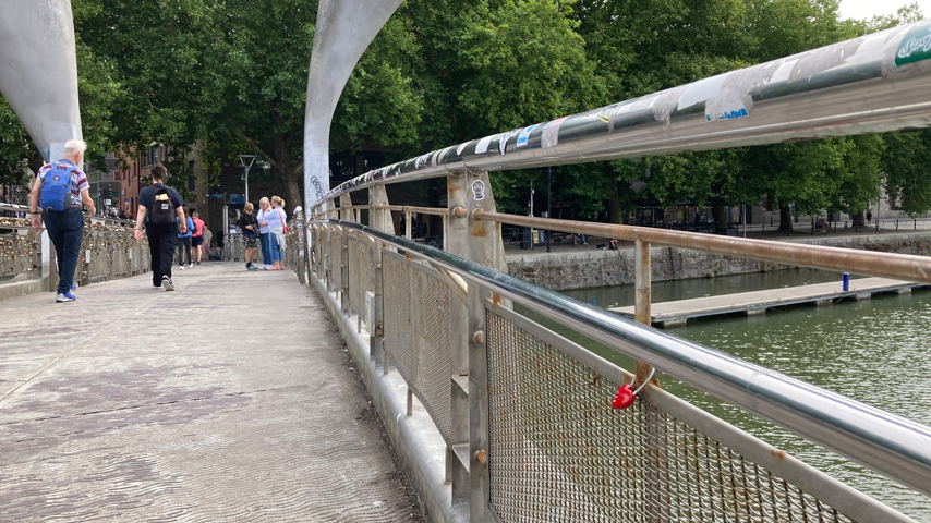 Pero's Bridge with the empty space which the padlocks were attached to. People are walking on the bridge towards Queen Square.