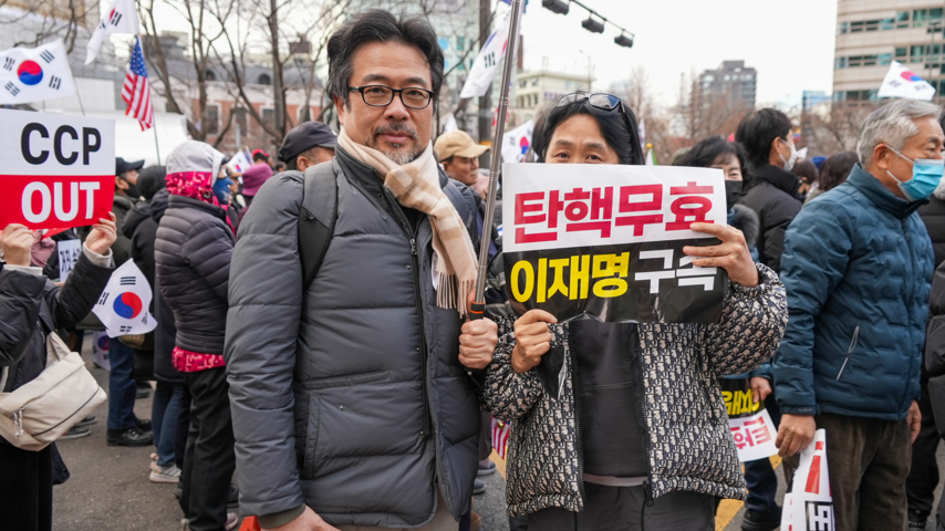 A man stands with a woman, who holds a sign saying that the impeachment was invalid