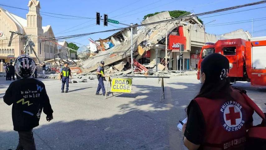 Red cross worker looks over collapsed building and road closure sign following earthquake
