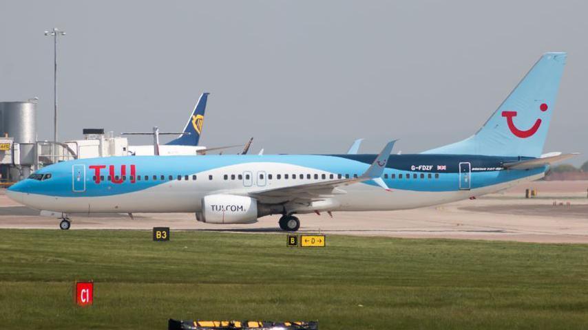 A Boeing 737-8K5, in sky blue TUI livery, sits on a runway at Manchester Airport.