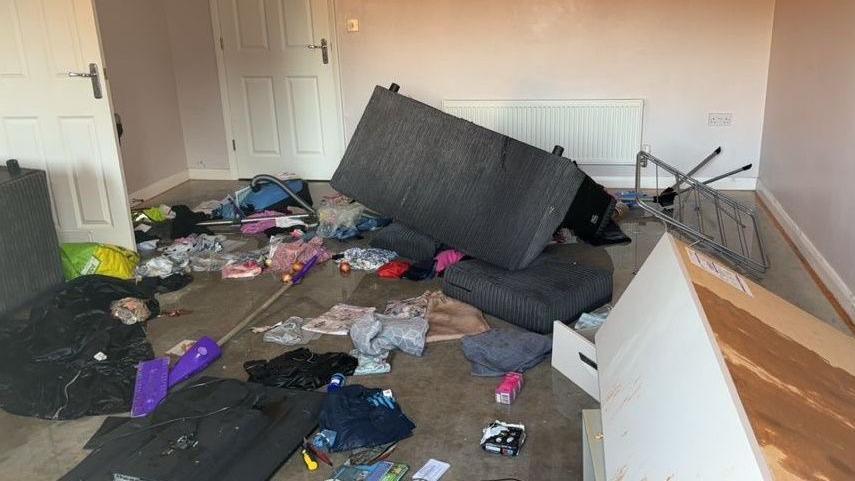 A ransacked room inside Courtney Mitchell's flat - a sofa can be seen overturned and there are piles of mess and clothing strewn across the floor.