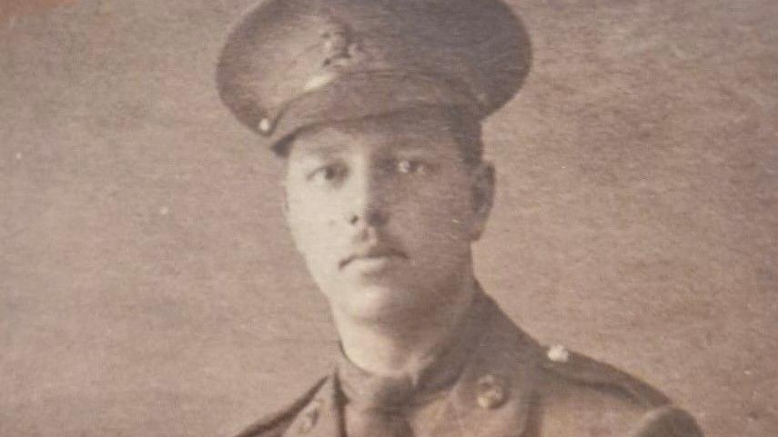 A black and white photograph of 2nd Lt Noel Whittles in uniform and cap, who has a neat moustache and looks into the camera with a serious expression