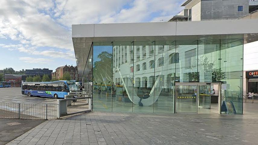 Blackburn's glass fronted bus station on a cloudy day showing a blue single decker bus parked at the front of the bus lanes.