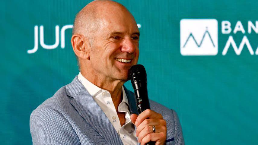 Adrian Newey speaking into a microphone at an Aston Martin news conference