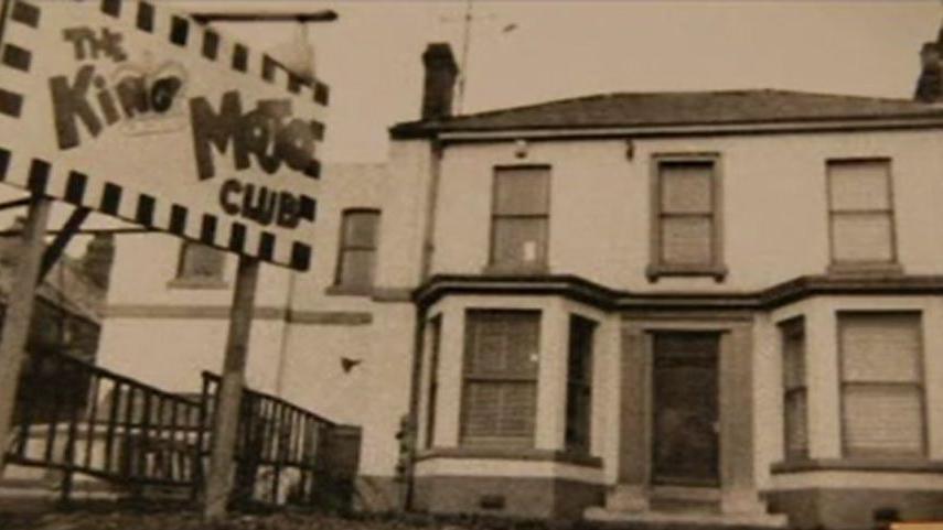 A sepia photograph of a Victorian building with a sign outside that reads "The King Mojo Club".