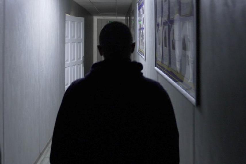 A rear view of the top half of Vlad in silhouette in a poorly-lit corridor of the Rivne detention centre. His head is shaven.