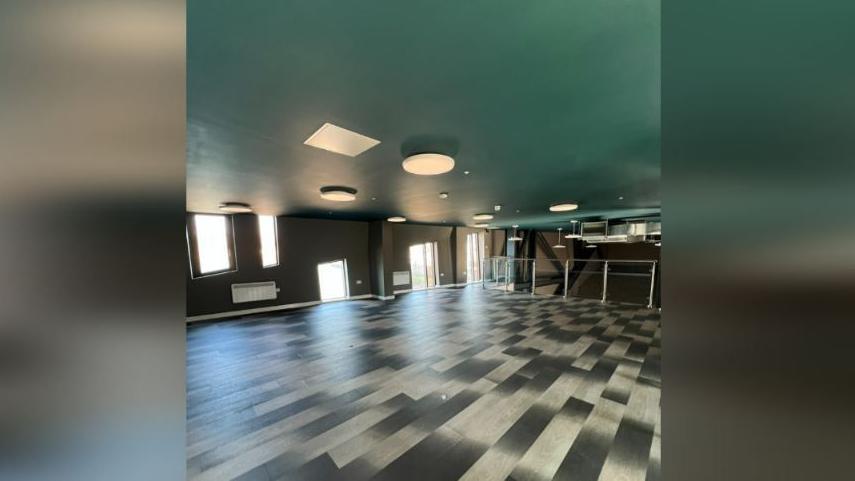 The mezzanine seating area. The room is empty. The walls are dark grey and the windows are of irregular shapes. The flooring in in a dark grey and off-white irregular pattern.