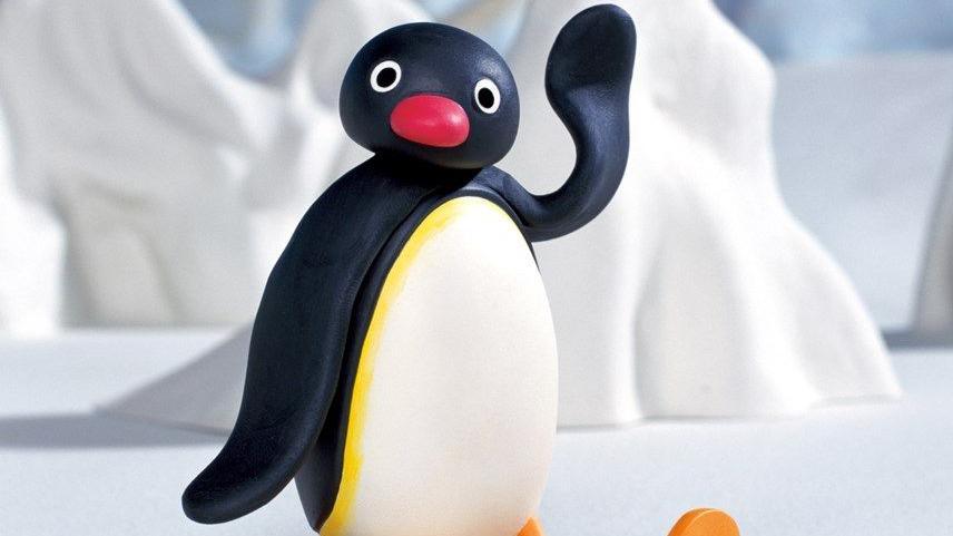 The animated penguin character, Pingu. He has a red nose. His arm is up above his head and snow covered peaks can be seen in the background. 