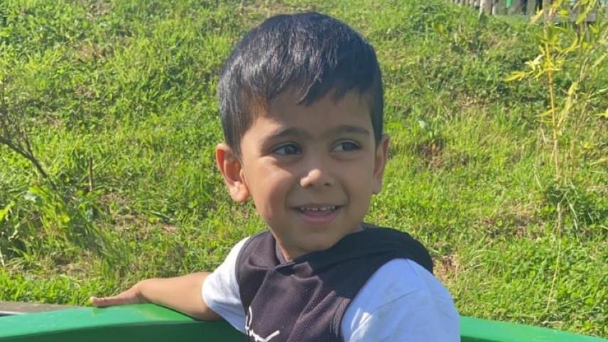 Yusuf Mahmud Nazir, pictured with short, dark hair. He has brown eyes. He is leaning on the back of a green seat and there is grass behind him.