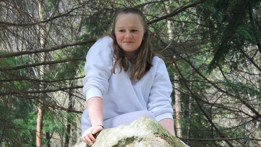 Jessica Baker in a wooded area with a slight smile on her face, wearing a light coloured top and her hair is loose around her face