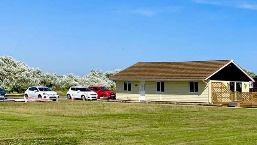 A yellow bungalow on flat ground with cars parked next to it