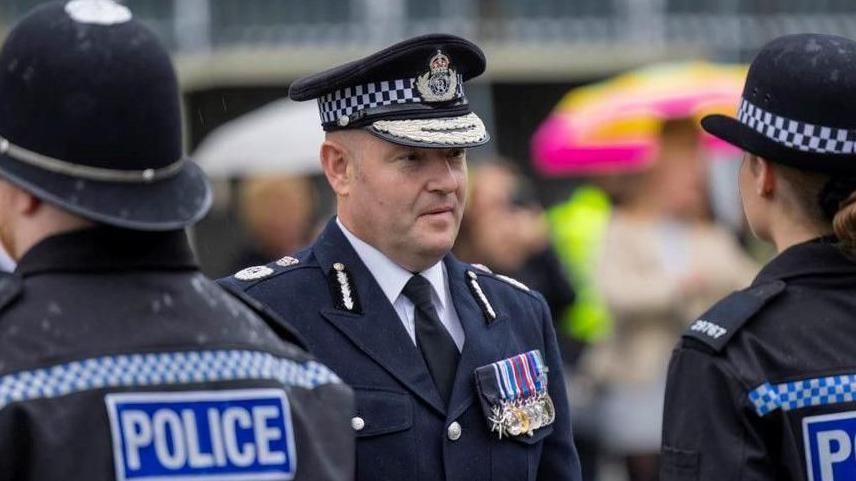 Craig Guildford looks at a line-up of police officers while dressed in full police uniform.