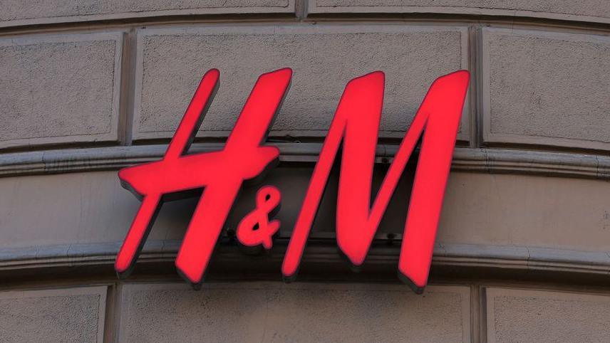 A red H&M sign is hung on a beige sandstone brick wall. 