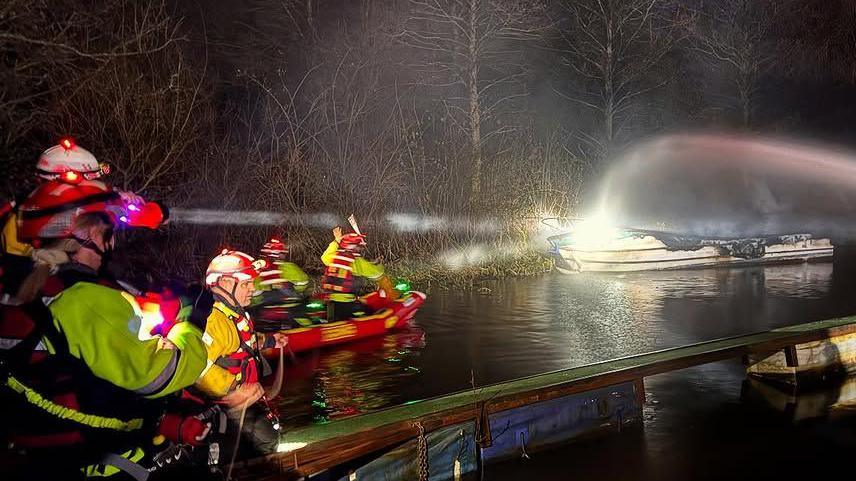 Firefighters use hosepipes to spray water onto a smoking pleasure boat