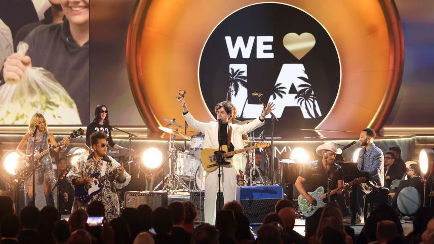 Dawes, John Legend, Brad Paisley, Sheryl Crow, Brittany Howard and St. Vincent preform on stage at the Grammys with a backdrop that reads "We love LA" after the wildfires in the city 