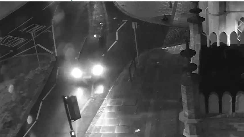 A black and white CCTV image of a car on a road.
