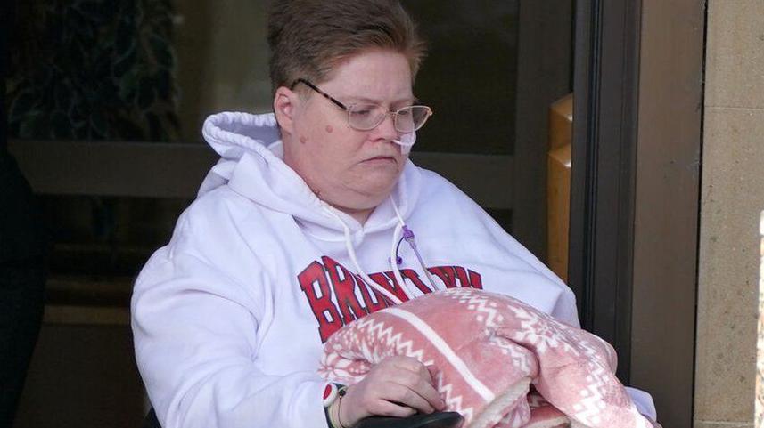 Woman wearing glasses and white hooded top in wheelchair