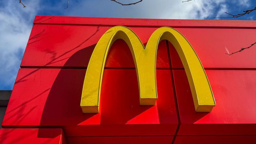 A red building with a yellow letter M on it. It is the logo for McDonald's.