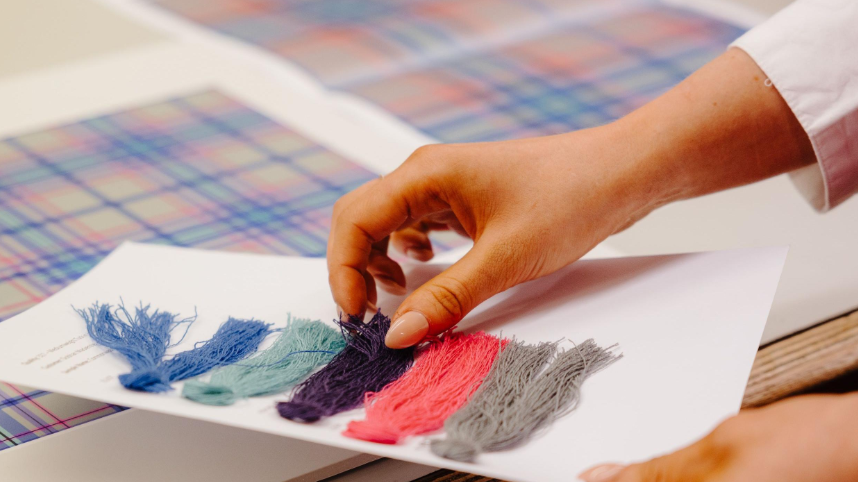 A close up of the designer's hands, touching the thread swatches over the tartan design.