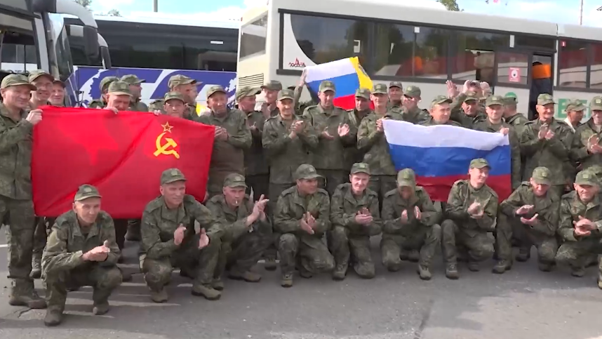 Men wearing Russian uniform gather for a photo holding Russian and Soviet flags
