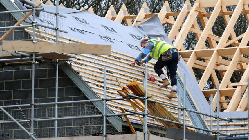 A man working on the roof of a house which is under construction 