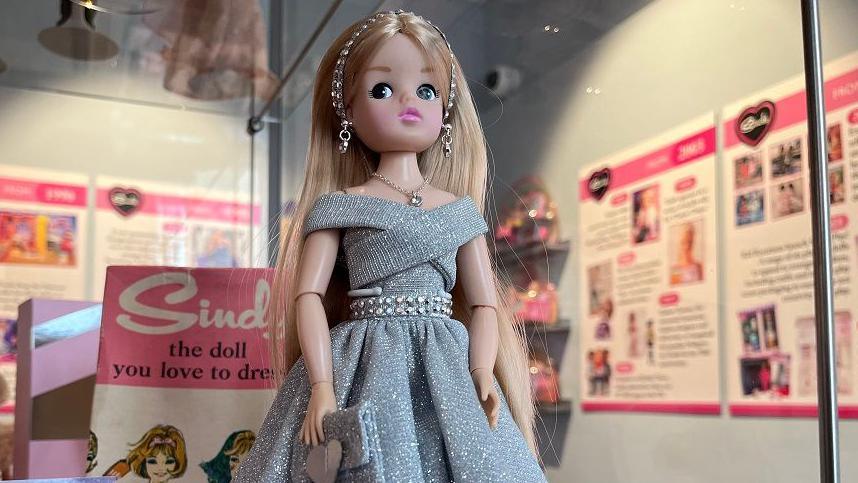 A doll with blonde hear wearing a silver glittery dress and headband