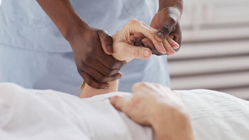 A black hospital worker holds the hand of an elderly white patient.