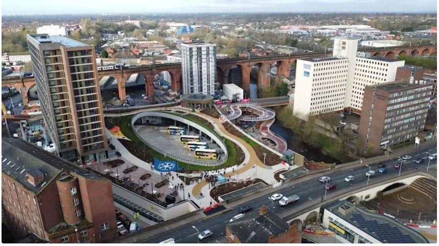 An aerial view image of Stockport Interchange. The new interchange features 18 bus stands, with a number of buses currently parked at the site. There are a number of high rise buildings and the historic viaduct is in the background.