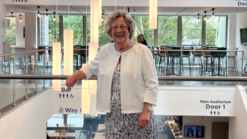 Councillor Connie Hockley  standing in the theatre foyer wearing a flowery dress and white jacket, smiling at the camera she has glasses on.