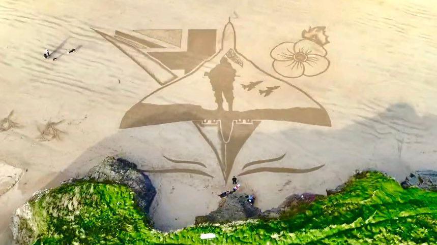 Overhead photo showing sand art of a Vulcan aircraft with a poppy, a soldier and union lags