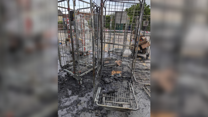 Tall metal cages on wheels usually used to take products around a supermarket with charred remains of boxes and ash around them.