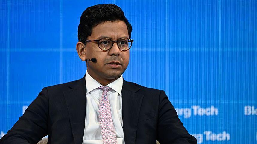 Kanishka Narayan sitting in a chair with a microphone. He is wearing a dark suit with a patterned tie.