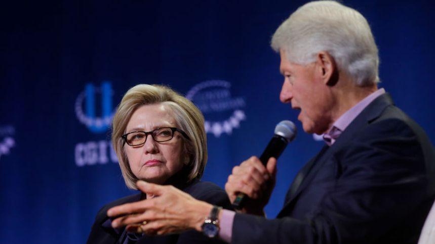 A file photo of Bill and Hillary Clinton on stage at an event - Bill is speaking into the microphone