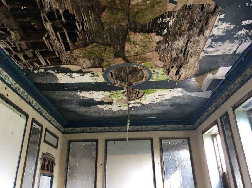 A badly damaged room interior with damaged panelling on the walls and ceiling battens visible where the plaster has come away.